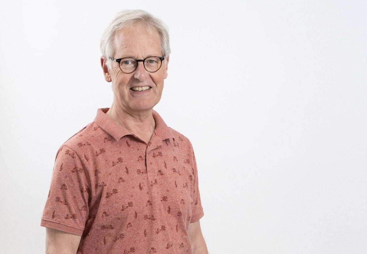 Een man met een bril en zijn hand in zijn zak en een apricotkleurig poloshirt