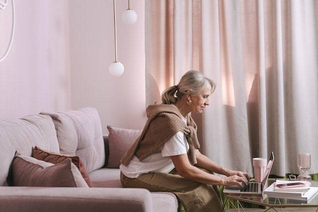 levenstestament afsluiten Een oudroze foto met een vrouw op een bank met oudroze kleding werkend aan haar laptop