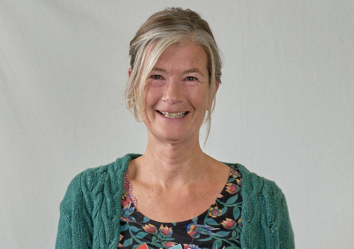 Een vrouw met grijsblond haar met een groen vest en kleurboeken in haar hand