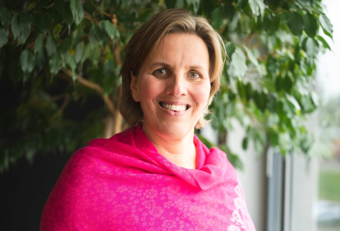 Een vrouw met halfkort haar en een roze omslagdoek staat voor een grote plant